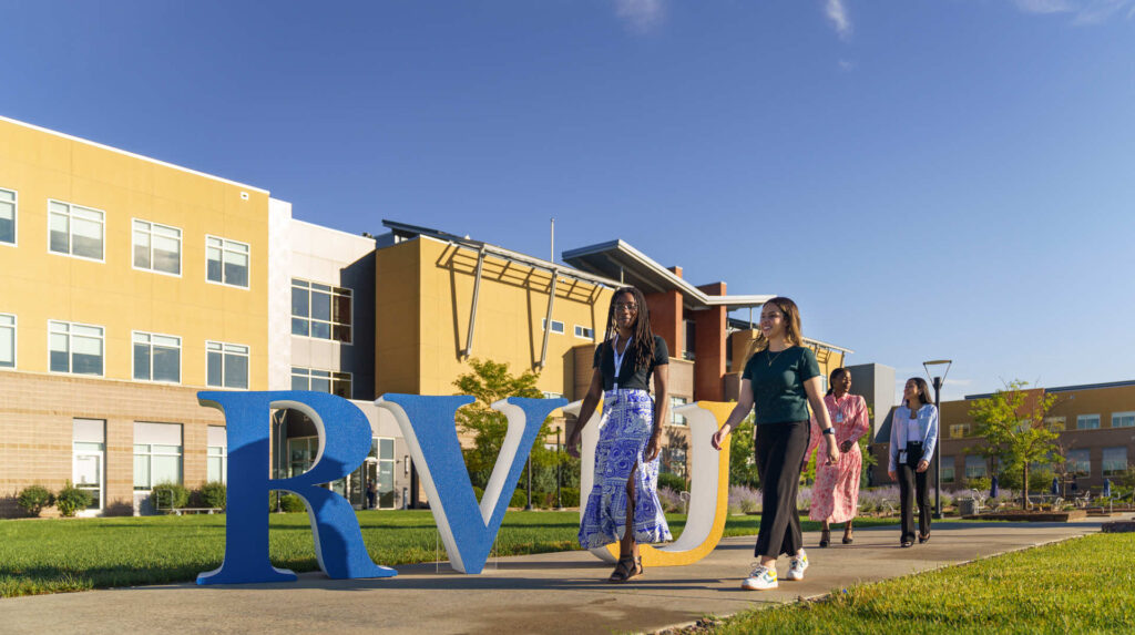 Students walking in front of RVU sign on grass.