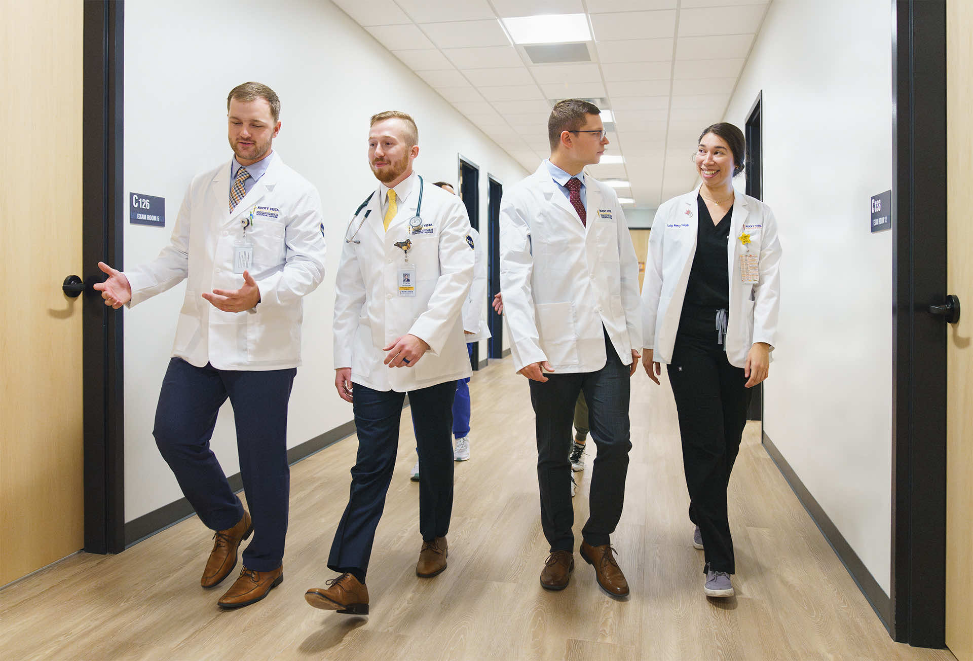 Med students wearing white coats walking down hallway.