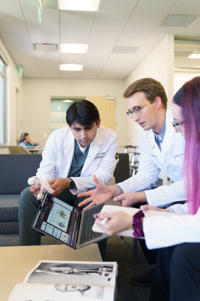 Three students wearing white coats looking at laptop. 